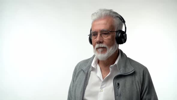 Stylish Emotional Old Man with a Gray Beard and Headphones Listens to Modern Music and Dances on a