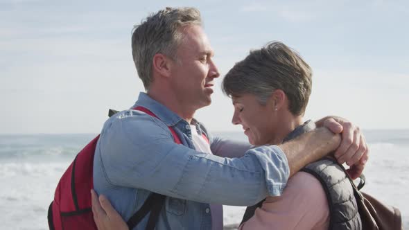 Caucasian couple enjoying free time by sea on sunny day embracing alt