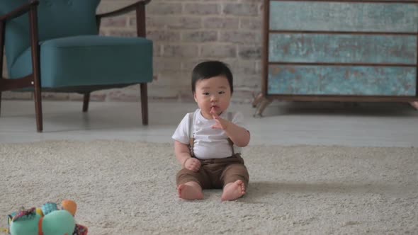 Small Asian boy child sits on the floor in the living room and looks at camera alt