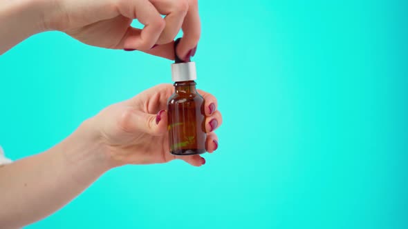 Female Hands Holding Bottle of Skincare Oil Against Blue Background alt
