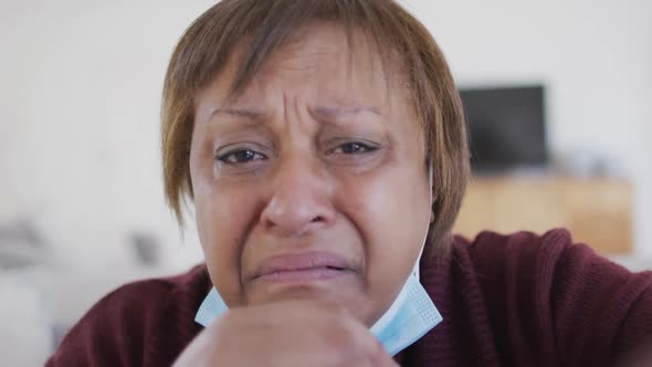 Distressed, sick african american senior woman with face mask making video call at home alt