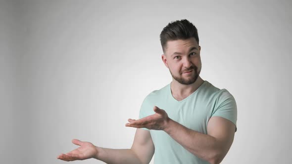 Emotional Man in Green Tshirt Points Aside on Empty Palm on Grey Background
