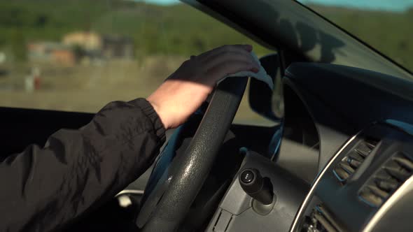 a Man Cleans the Steering Wheel with Disinfectant Wet Wipes While Sitting in the Car alt