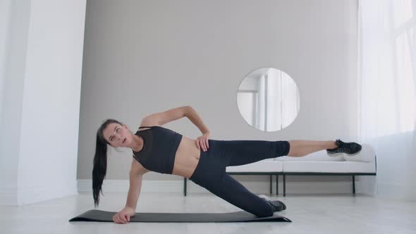 The Brunette in the Apartment Does an Exercise Lateral Plank Standing on Her Knee alt