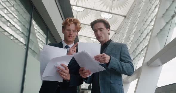 Two Businessmen are Discussing a Business Plan for Growth of Sales Looking in Papers Standing alt