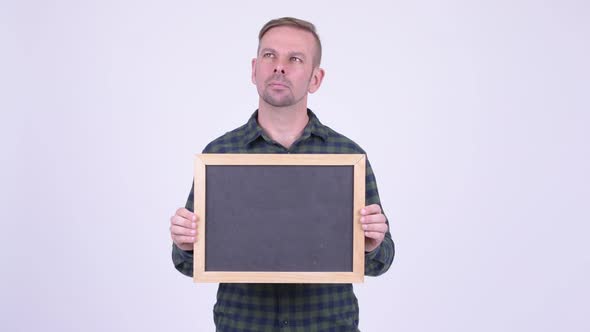 Portrait of Happy Blonde Hipster Man Thinking While Holding Blackboard alt