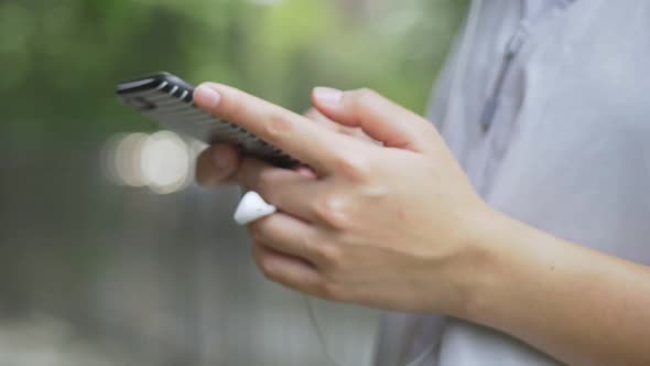 Asian woman fitness runner using mobile phone listening music at a public park.