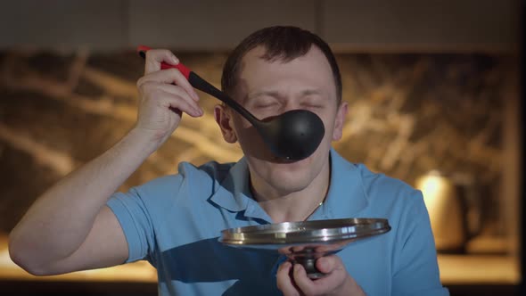 Man with a Ladle Stands in Front of the Kitchen Tasting Food From the Ladle Sampling the Food alt