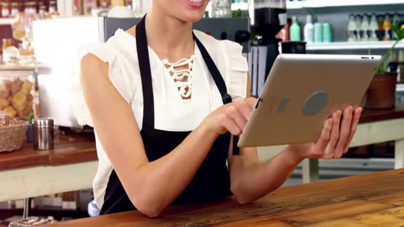 Smiling waitress standing at counter using digital tablet alt