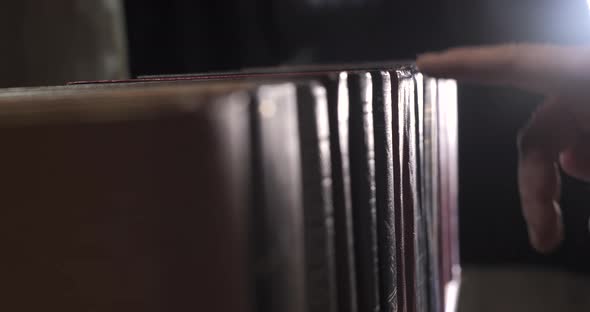 A Mans Hand is Looking for the Right Book Among a Collection of Volumes alt