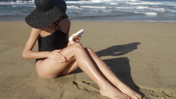 Young woman applying sun cream on beach alt