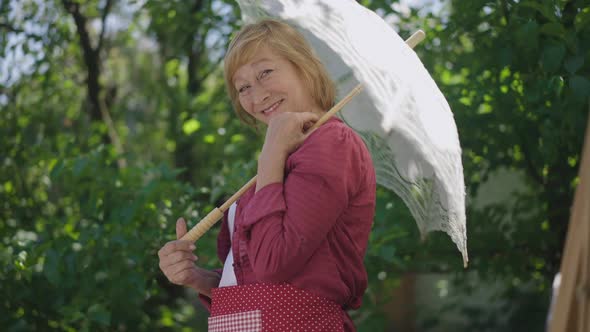 Charming Talented Senior Woman Posing with Sun Umbrella at Easel in Slow Motion alt