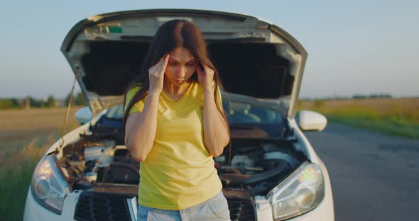 Young Upset Girl Standing Near Car with Hood Open alt