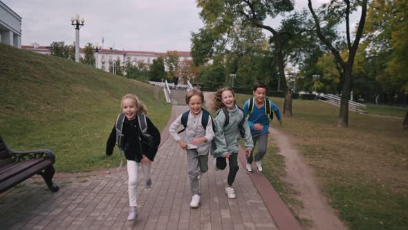 Front View of Caucasian Schoolkids with Schoolbags Running in the School Yard at School alt