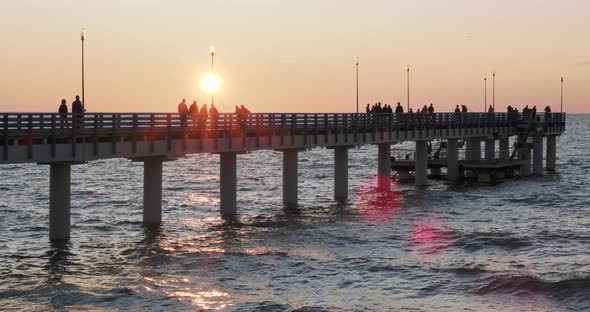 Silhouettes of People Walking on the Pier Against the Sunset. Local People Are Fishing, Tourists Are alt
