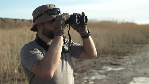 Side View of Bearded Adult Man Hunter of a Guard in Military Tshirt and Hat Looking Through alt