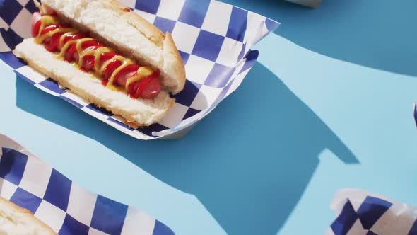 Video of hot dogs with mustard and ketchup on a blue surface alt