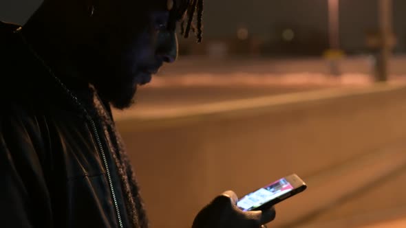 young african man sitting outdoor and looking the smartphone alt
