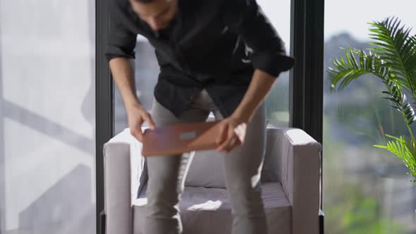 Young Middle Eastern Serious Man Walking to Armchair at Window Sitting Down and Opening Laptop alt