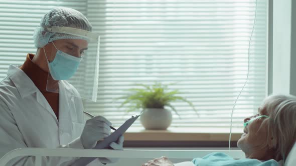 Doctor in Protective Uniform Visiting Elderly Woman in Hospital Ward alt