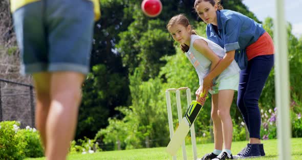 Family playing cricket in park alt