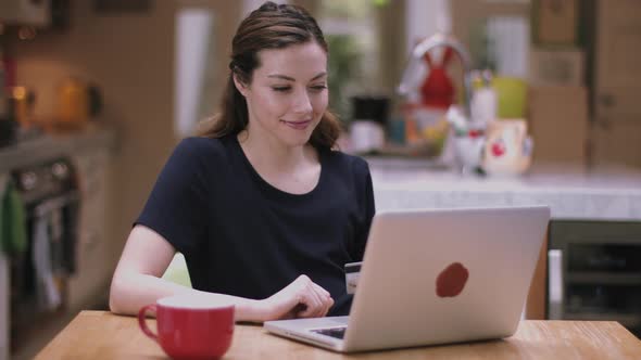 Young adult woman buying online using laptop in kitchen