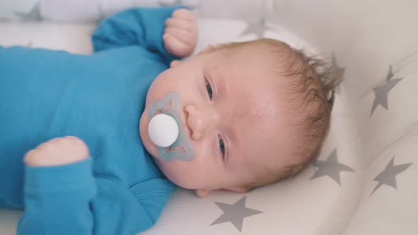 Happy Newborn Baby Sucks Dummy in Cocoon in Rocking Cot alt