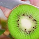 Man Hands with Knife Cut Off a Round Piece of Kiwi