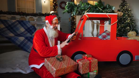 Santa Claus Makes List of Presents Using Tablet.