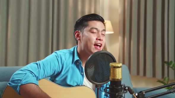 Asian Man Playing Guitar And Sing A Song While Live Streaming For His Social Media Channel alt