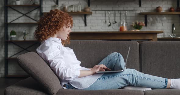 Side View of Upset Young Woman Looking at Laptop Screen and Reading Bad Message While Sitting on alt