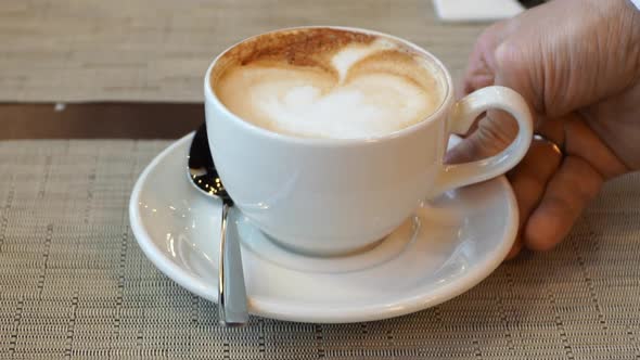 Close Up of Waiters Hand Puts Down Cup of Cappuccino Coffee with Saucer and Spoon on Table in Cafe