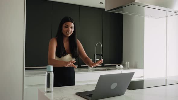 Young Darkskinned Brunette in the Kitchen with a Laptop Video Chatting alt