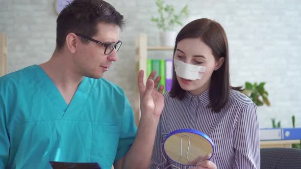 Man Doctor Plastic Surgeon Talks To a Young Woman After Plastic Surgery on the Face alt