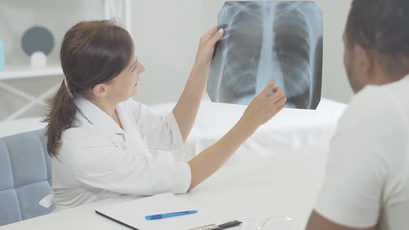 Doctor and Patient Examining Lungs X-ray in Hospital. African American Man and Caucasian Woman alt