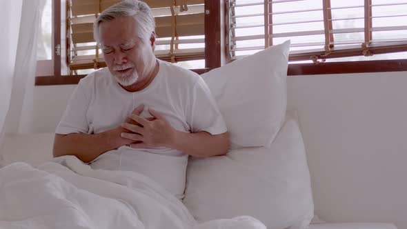 Elderly Asian man Heart pain due to heart disease in bed room. alt