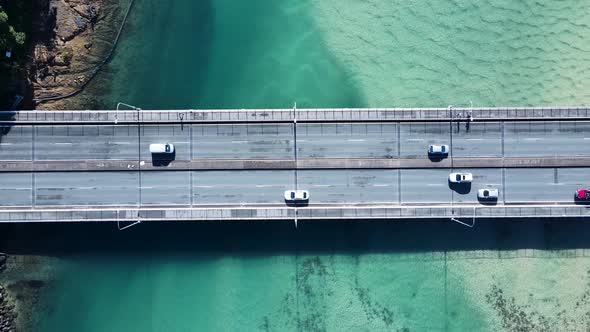 Busy coastal road and pedestrian bridge spanning a clear ocean estuary allowing people and vehicles alt