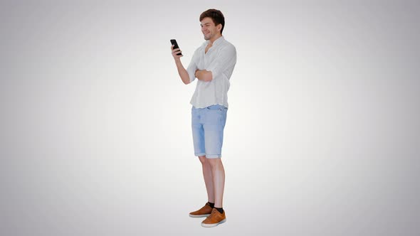 Handsome Young Man Using His Smartphone and Laughing on Gradient Background alt