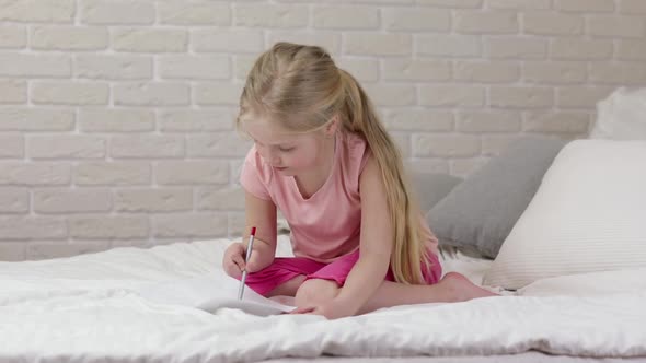 Cute Little Girl Drawing Pictures While Lying on Bed