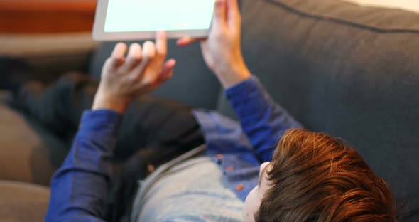 Man lying on sofa and using digital tablet in living room alt