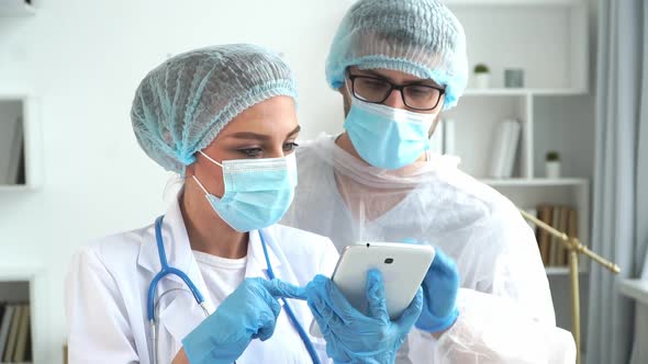 Doctors in White Coats and Masks Discuss Work on Digital Tablet in Clinic