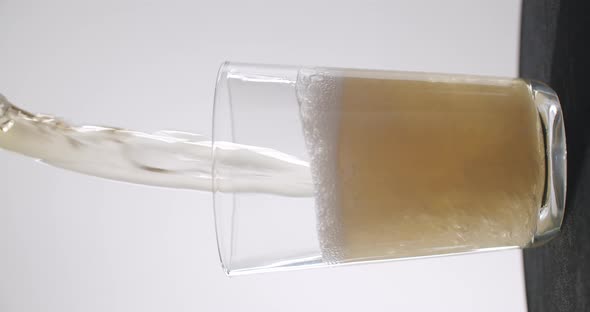 Close up shot of beer getting poured fast into a glass. White background, 50fps, vertical video. alt