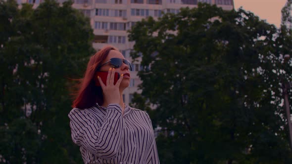 Young Woman in Sunglasses with Mobile Phone on Street in Summertime alt
