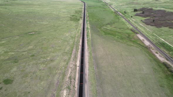 Aerial tilt up revealing back of long coal train traveling away from Colorado mountains. alt