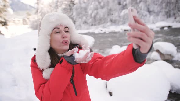 Happy Woman in a Red Jacket and a Fur Hat Sits in a Mountain River in the Winter Forest and Talking alt