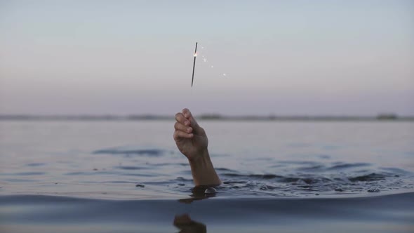 Man's Hand From the Water Holding a Sparkler