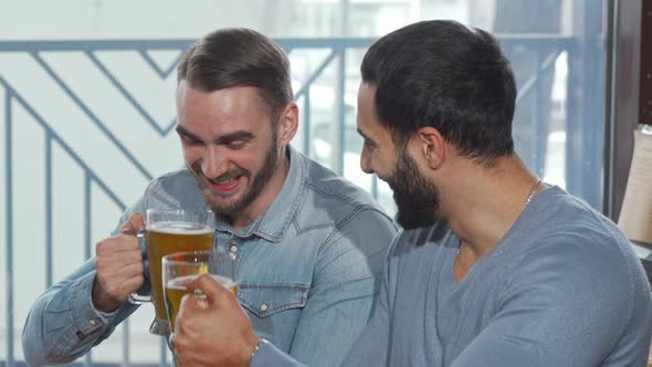 Happy Male Friends Clinking Beer Glasses Enjoying Drinking at the Pub