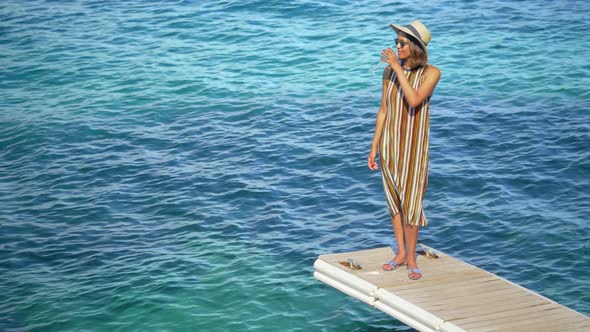 A woman with a glass of white wine on a dock over the Mediterranean Sea in Italy, Europe alt