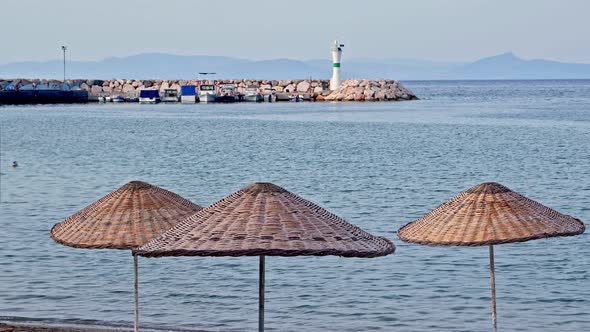 Straw Umbrellas On The Beach And People Swimming In The Sea alt