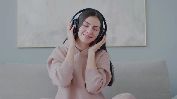 Young woman sitting in wireless headphones moving and dancing to beat of music.